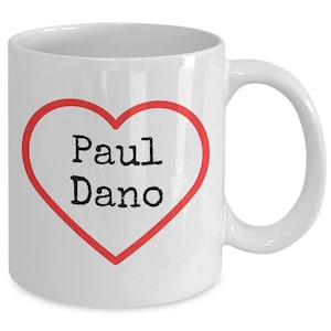 May include: White ceramic coffee mug with a red heart outline and the text "Paul Dano" inside the heart.