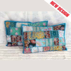 Puede incluir: Dos cojines rectangulares de patchwork. Los cojines presentan una variedad de cuadrados de tela coloridos en tonos turquesa, rosa y dorado, con un borde turquesa. El texto "NEW DESIGN" está en la esquina superior derecha.