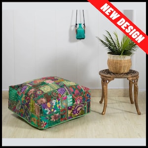May include: A square patchwork pouffe with a green base and a variety of colourful floral and geometric patterns. The pouffe is on a light wood floor. A small, ornate side table with a potted plant and a turquoise vase hanging on the wall.