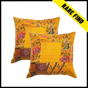 May include: Two square decorative pillows with a patchwork design. The pillows are primarily yellow with patches of red, green, and orange. The pillows have a stitched pattern and the text "RARE FIND" is visible in the upper right corner.