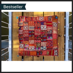 May include: A patchwork cushion with a vibrant mix of red, orange, and patterned fabric squares. The cushion is trimmed with a decorative border and small tassels. The word "Bestseller" is displayed in a banner.