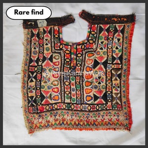 Puede incluir: Textil vintage bordado con intrincados diseños en una variedad de colores, incluyendo rojo, naranja, verde y negro. El textil presenta patrones geométricos y florales, con el texto "Rare find" en un óvalo blanco. Probablemente sea una prenda de vestir o un objeto decorativo.