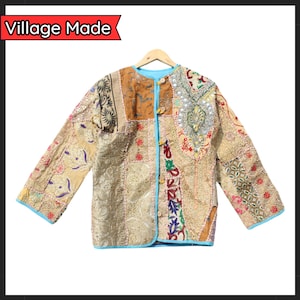 May include: A patchwork jacket in gold, brown, and cream tones, featuring various patterned fabrics. It has a light blue trim and button closures. The text "Village Made" is visible in the upper left corner.
