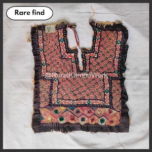 Puede incluir: Textil vintage cosido a mano con intrincados bordados en tonos rojos, rosas, verdes y amarillos. El textil presenta un patrón floral geométrico y está bordeado con un borde marrón oscuro. El texto "Rare find" está en un óvalo blanco.