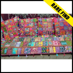 Puede incluir: Un juego de cuatro cojines decorativos y una funda de sofá a juego. Los cojines y la funda presentan un diseño de patchwork con colores vibrantes y patrones intrincados. Cada cojín tiene forma cuadrada con borlas en las esquinas. La funda del sofá es rectangular.