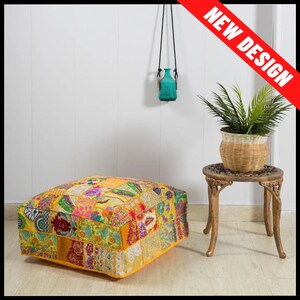 May include: A square, patchwork pouf with a yellow base and a variety of colorful fabric patches. A small, ornate side table holds a potted plant. A turquoise vase hangs from the wall. The words "NEW DESIGN" are in a red banner.