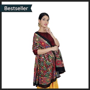 May include: A woman wearing a maroon top and a colourful embroidered shawl. The shawl features intricate patterns in red, green, yellow, and blue, with small mirror accents. The word "Bestseller" is in the top left corner.