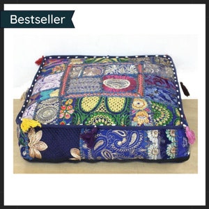 May include: Square floor cushion with a patchwork design in shades of blue, gold, and various colors. The cushion features embroidered floral and paisley patterns, with decorative tassels on the corners. The word "Bestseller" is in the top left corner.