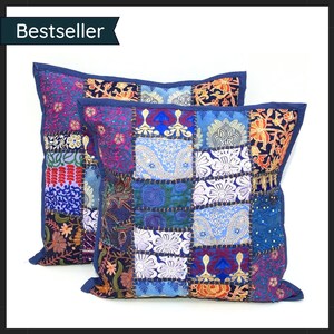 May include: Two square patchwork cushions with a variety of colourful fabric squares. The cushions feature a mix of floral and geometric patterns in shades of blue, purple, and orange. The cushions have a dark blue border and the word "Bestseller" is in the upper left corner.