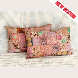 May include: Two rectangular decorative pillows with patchwork designs in shades of pink, peach, and beige. The pillows feature a variety of fabric patterns and textures, with a brown border. The words "NEW DESIGN" are in red text in the upper right corner.