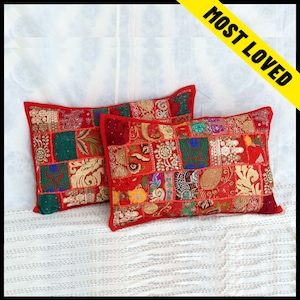 Peut inclure: Deux coussins rectangulaires avec un motif patchwork. Les coussins présentent une bordure rouge et un mélange de couleurs vives, notamment le rouge, le vert, l'or et le bleu. Le patchwork est composé de divers tissus avec des détails brodés.