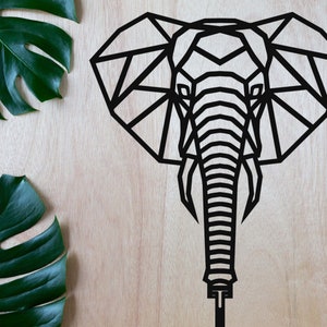Può includere: Silhouette di testa di elefante nera geometrica su uno sfondo in legno chiaro. La testa dell'elefante è composta da triangoli e linee.