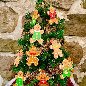 Könnte beinhalten: Ein kleiner Weihnachtsbaum, der mit Lebkuchenmann-Ornamenten geschmückt ist. Der Baum hat einen goldenen Stern an der Spitze und einen rot-weißen Baumrock. Die Lebkuchenmänner sind mit farbenfrohem Zuckerguss und Kleidung verziert.
