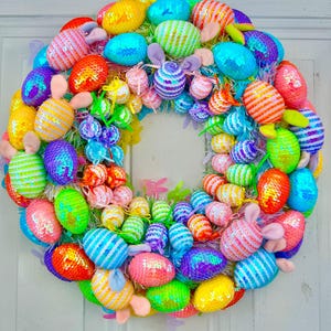 May include: A colorful Easter wreath featuring a variety of sequined eggs in shades of yellow, blue, green, orange, pink, and purple. Some eggs have bunny ears attached. The wreath is a festive decoration for the spring season.