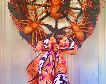 May include: A Halloween wreath with a woven brown base, adorned with orange glitter spiders, black bats, and a spiderweb design. A large bow with orange, white, and purple ribbons with Halloween-themed text and spiderweb patterns completes the festive look.