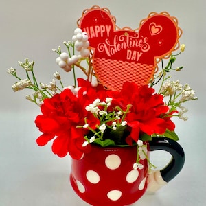 May include: Red polka dot mug with a bouquet of red flowers and white baby's breath. A red and white Mickey Mouse shaped card with the text "Happy Valentine's Day" is in the bouquet.