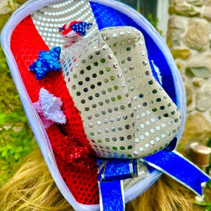 May include: A red, white, and blue sequined cowboy hat with a blue ribbon. The hat is decorated with stars and other patriotic embellishments.