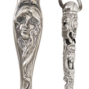 Peut inclure: Deux ustensiles de service anciens en argent. L'un présente un visage de femme avec des cheveux fluides, l'autre a un design orné avec une boucle en haut. Les ustensiles sont probablement destinés à servir des aliments.