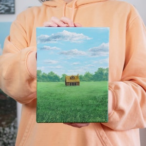 Può includere: Un dipinto che rappresenta una piccola casa marrone con un tetto di paglia in un campo verde. La casa ha una sola finestra e un camino. Il cielo è blu con nuvole bianche.
