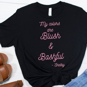 May include: Black t-shirt with the text "My colours are Blush & Bashful - Shelby" in pink lettering.
