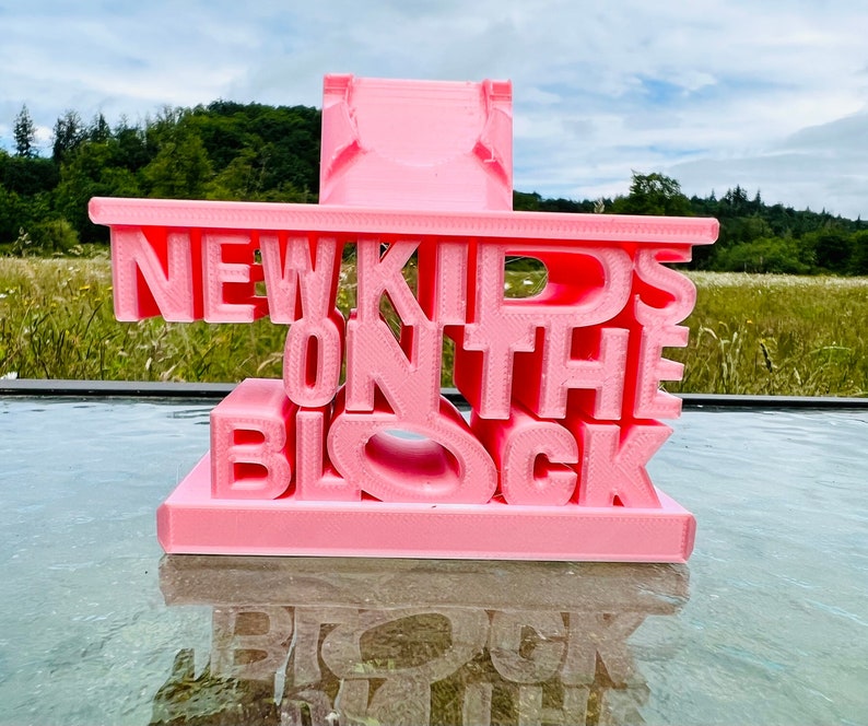 May include: A pink 3D printed sign that reads "NEW KIDS ON THE BLOCK".
