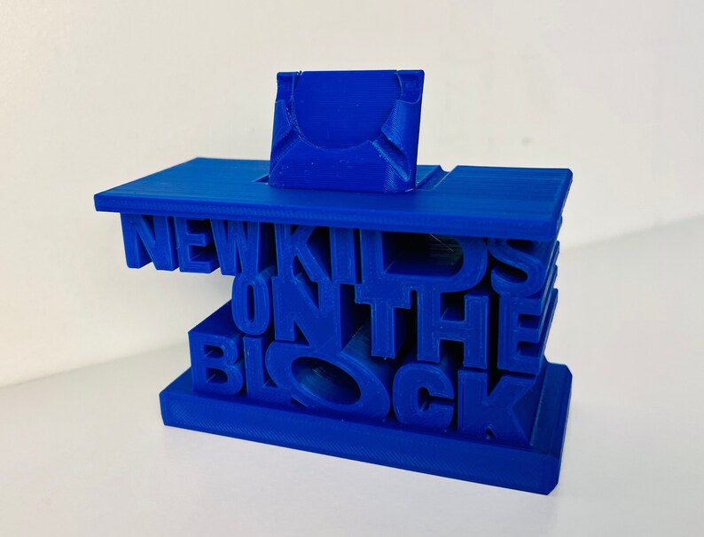 May include: A blue 3D printed model of the words "New Kids on the Block" with a small blue rectangular block on top.
