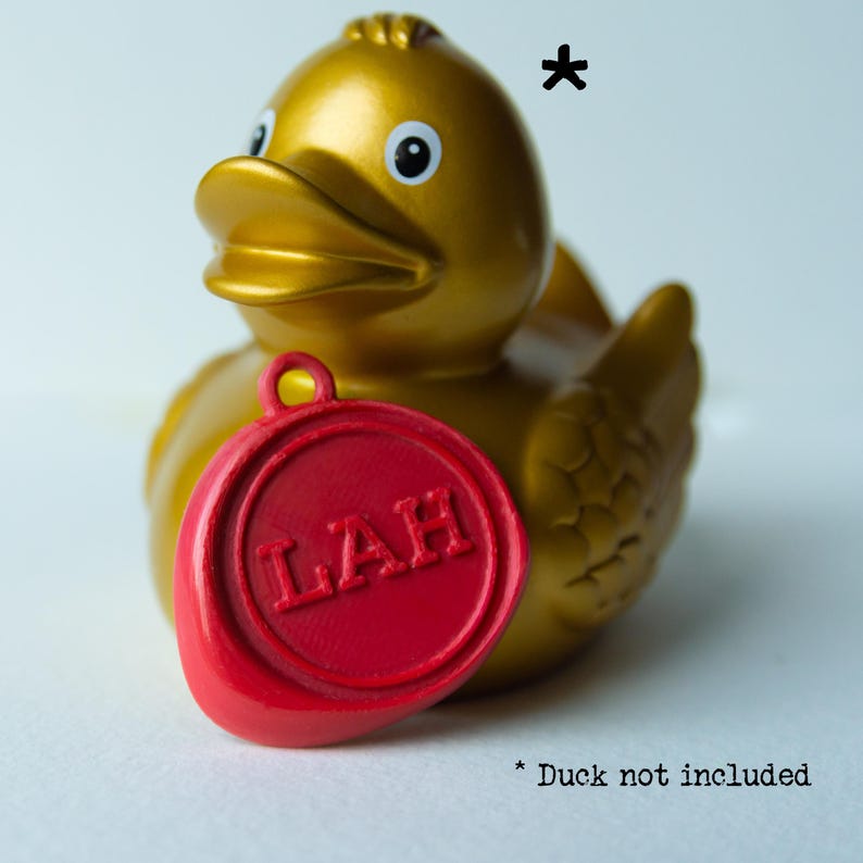 Red wax seal keyring in the style of Taskmaster with the initials LAH leaning against a gold rubber duck and text Duck not included