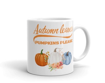 Könnte beinhalten: Eine weiße Keramiktasse mit dem Text "Autumn leaves pumpkins please" in Orange. Die Tasse zeigt einen weißen Kürbis, einen orangefarbenen Kürbis und einen blauen Kürbis mit floralen Akzenten.