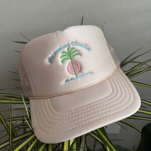 Pode incluir: Boné de caminhoneiro bege com parte traseira em malha e aba curva. O boné apresenta um design bordado de uma palmeira, sol e ondas, com as palavras "permanent vacation" em itálico. O boné tem um detalhe de corda ao longo da aba.