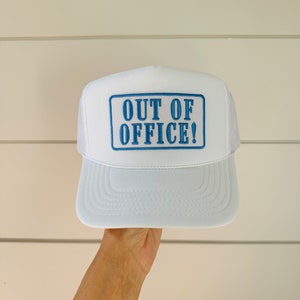 May include: White trucker hat with a blue rectangular patch that reads "OUT OF OFFICE!" in a bold, sans-serif font. The hat has a white mesh back and a curved brim. A fun accessory for casual wear.