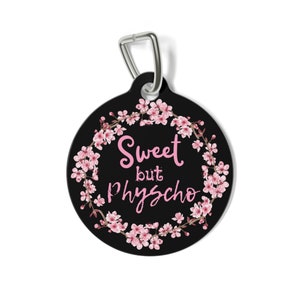 May include: Black round tag with a pink floral wreath and the text "Sweet but Psycho" in pink lettering. The tag has a silver metal loop.