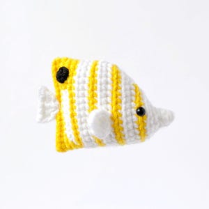 May include: A crocheted yellow and white striped fish with black eyes. The fish has a white fin on each side and a white tail fin.