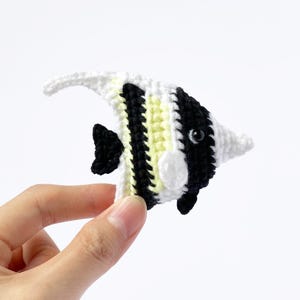 May include: A crocheted black, white, and yellow angelfish with a black eye. The angelfish is a small, handmade toy.