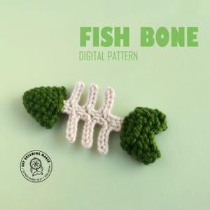 May include: A crocheted fish bone toy with a white bone and green fins. The toy is on a light green background. The text "FISH BONE DIGITAL PATTERN" is above the toy.