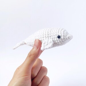 May include: A white crocheted beluga whale stuffed animal with black eyes.