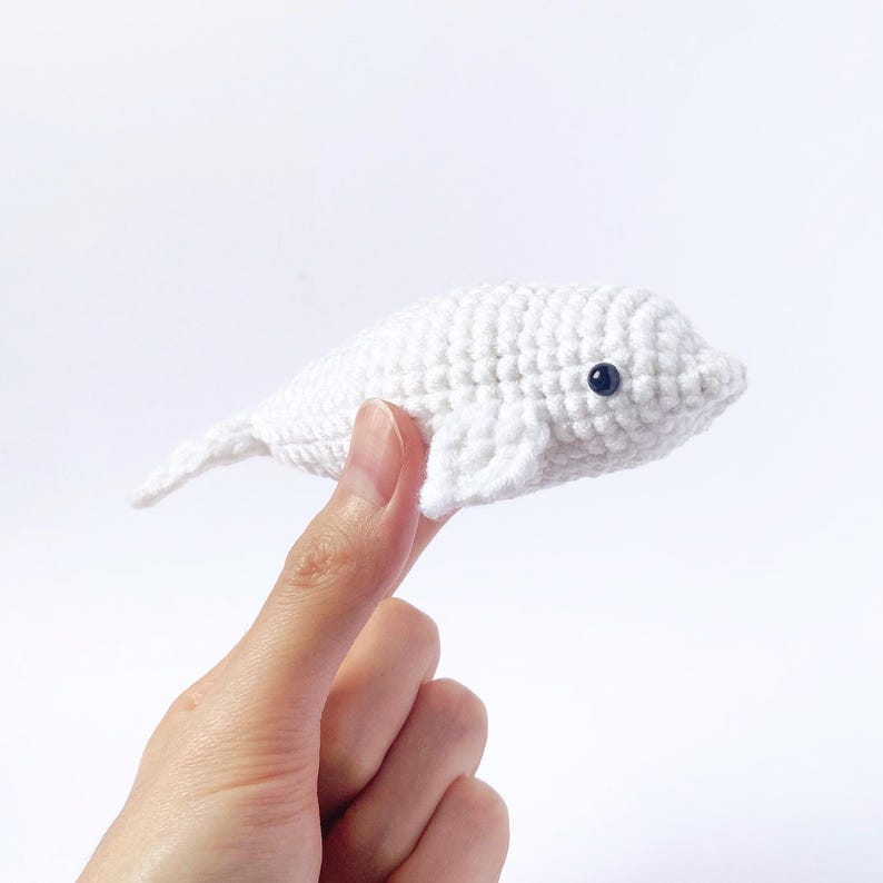 May include: A white crocheted beluga whale stuffed animal with black eyes.