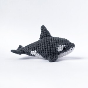 May include: A crocheted stuffed orca whale toy with black and white coloring. The orca has a white patch around its eye and a white patch on its belly.