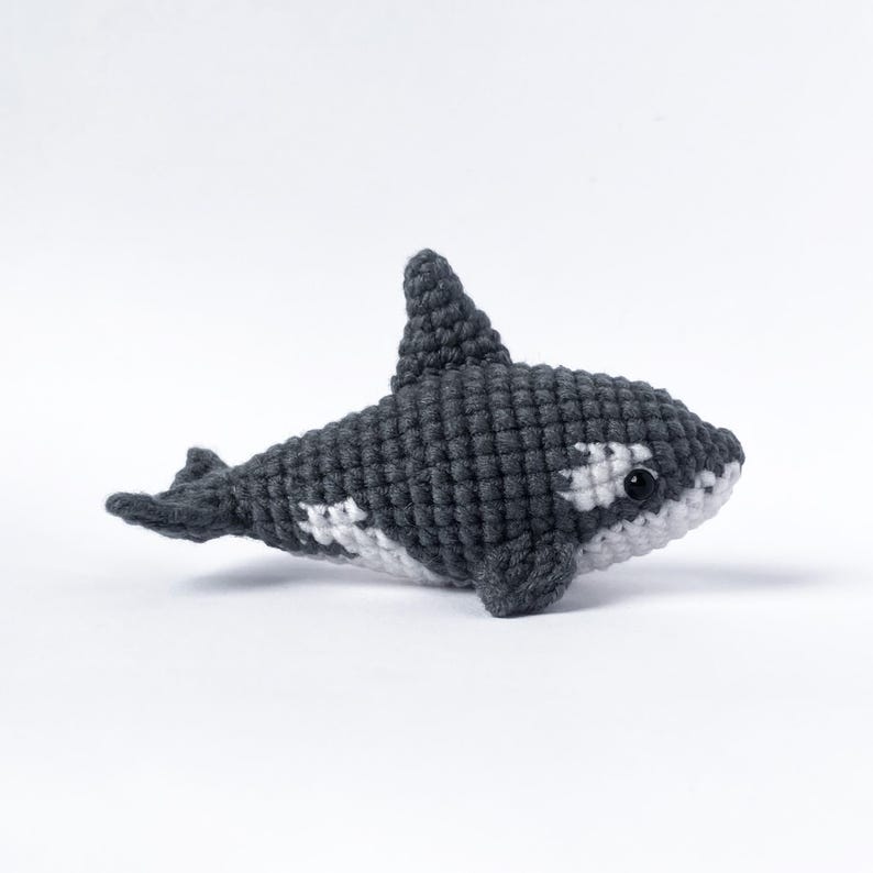 May include: A crocheted stuffed orca whale toy with black and white coloring. The orca has a white patch around its eye and a white patch on its belly.