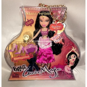 Könnte beinhalten: Bratz Genie Magic Puppe in einer transparenten Kunststoffverpackung. Die Puppe hat schwarzes Haar, ein rosa-goldenes Outfit und eine Halskette. Die Verpackung enthält ein zusätzliches Outfit und den Text "Bratz Genie Magic".