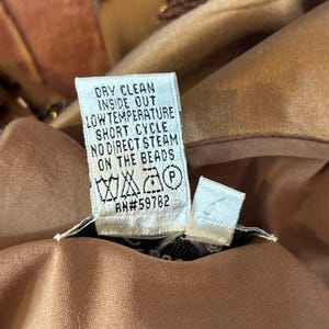 May include: Close-up of a garment care label with the text "DRY CLEAN INSIDE OUT LOW TEMPERATURE SHORT CYCLE NO DIRECT STEAM ON THE BEADS". The label also includes care symbols and the number RN#59782.