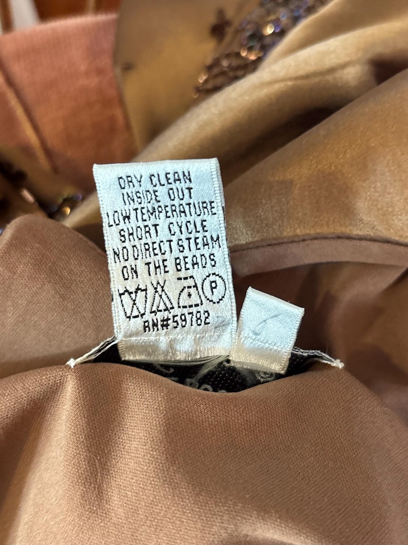 May include: Close-up of a garment care label with the text "DRY CLEAN INSIDE OUT LOW TEMPERATURE SHORT CYCLE NO DIRECT STEAM ON THE BEADS". The label also includes care symbols and the number RN#59782.