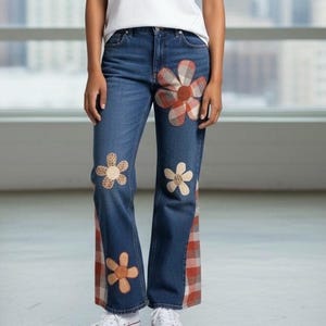 May include: Blue denim jeans with floral and plaid patchwork details. The jeans feature large flower appliqués in various colors and patterns, with plaid accents on the sides. A stylish and unique fashion item.