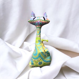 May include: A colorful, handmade cat toy with a green, blue, and purple paisley pattern. The cat has large, white eyes and a long, thin body.