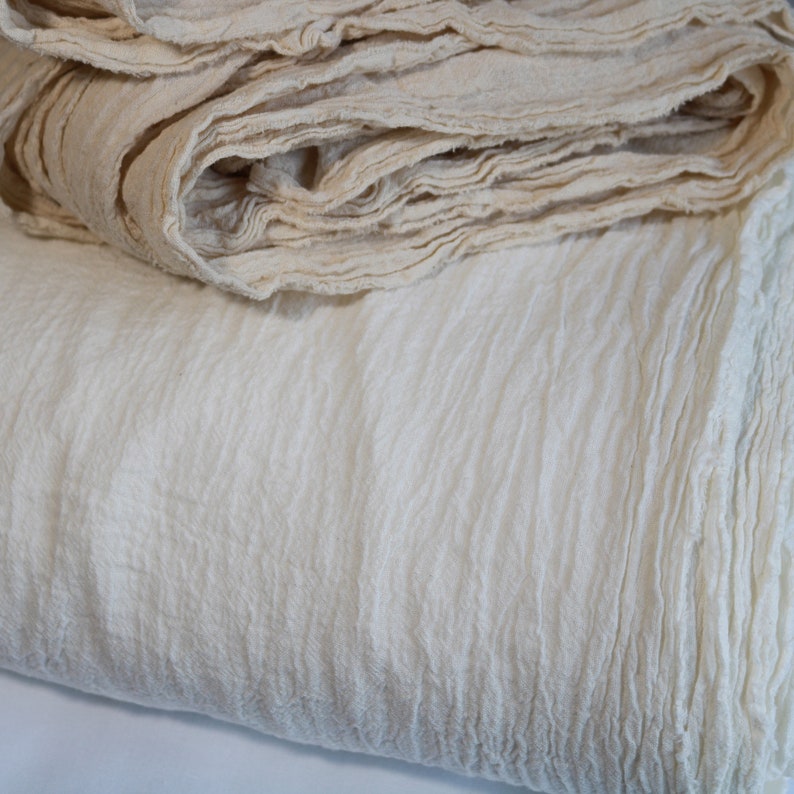 May include: A close-up of a white, textured fabric. The fabric is folded and layered, creating a soft and inviting look.