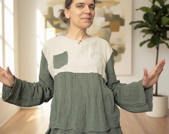 May include: A long-sleeved, color-blocked top in sage green and off-white. The top features a small pocket on the chest and a loose, flowing design. The sleeves are wide and flared. The fabric appears to be a textured cotton or linen blend.