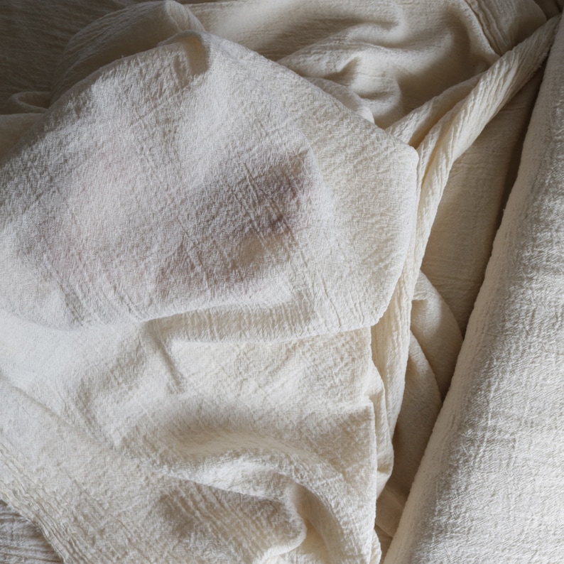 May include: A close-up of a white, textured fabric with a soft, crinkled appearance. The fabric is folded and draped, creating a sense of depth and dimension.