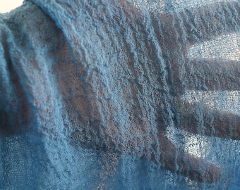 May include: A close-up of a light blue, textured fabric with a loose weave. The fabric is draped over a hand, creating a soft, flowing effect.