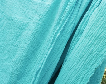 May include: Close-up of a light blue fabric with a textured, crinkled surface. The fabric is folded in half, creating a diagonal line.