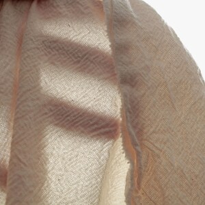 May include: Close-up of a pale pink fabric with a woven texture. The fabric is folded over itself, creating a layered effect.