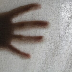Puede incluir: Un primer plano de la sombra de una mano proyectada sobre una superficie blanca texturizada.